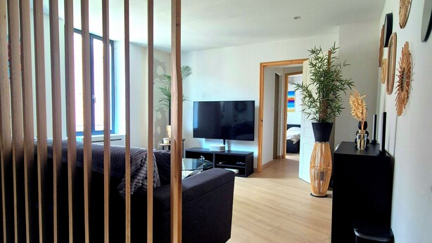 Una sala moderna con un sofá, un televisor, una planta en maceta y un elemento decorativo en la pared.