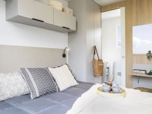 Een moderne slaapkamer met een grijze bank, kussens met een patroon, een nachtkastje met een lamp en een spiegel.