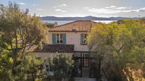 Eine Villa im mediterranen Stil mit einem Ziegeldach, grünen Fensterläden und Blick auf das Meer und die Hügel.