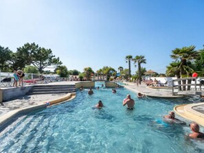 Ett poolområde med flera pooler, trappsteg som leder ner i vattnet och folk som badar.