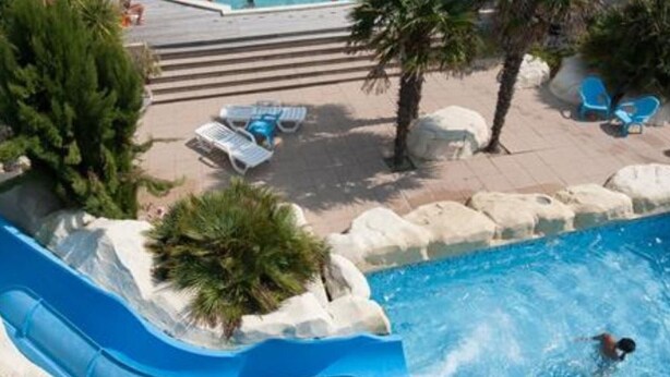 A pool with a blue slide, palm trees, and lounge chairs. - Mobile home, pets welcome - 5 guests (Saint-Jean-de-Monts)