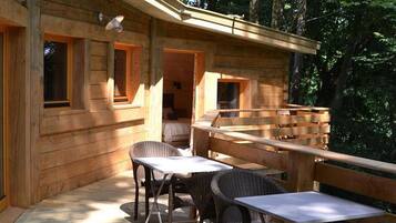 Una cabaña de madera con terraza, sillas de mimbre y una mesa.