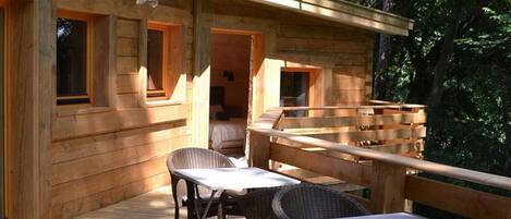Una cabaña de madera con terraza, sillas de mimbre y una mesa.