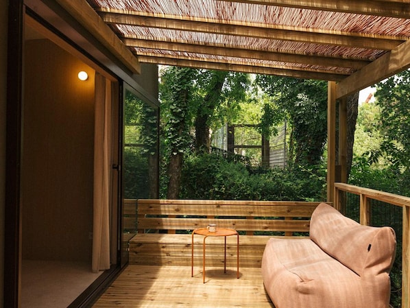 A wooden deck with a bench and a table, a wooden railing, and a view of a lush green garden.