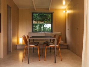 A dining area with a table and chairs, a bench, a window with a view of greenery, and a wall-mounted light.