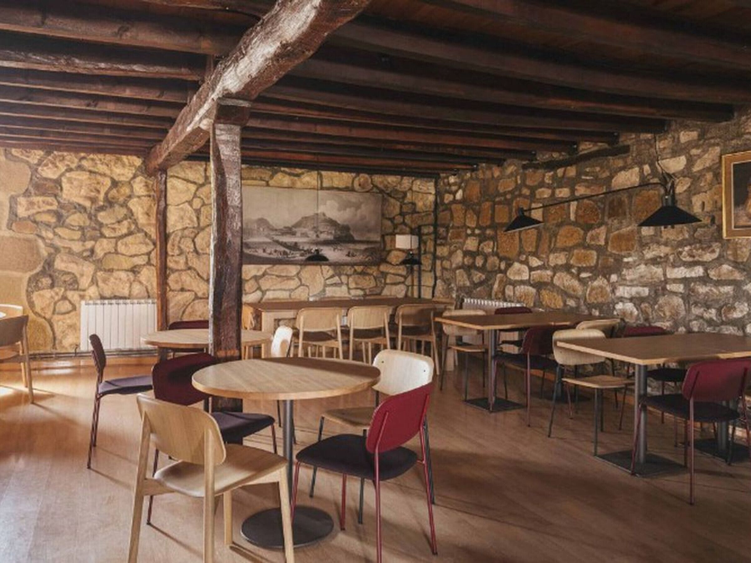 A rustic interior with stone walls, wooden tables, and chairs.