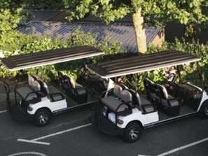 A row of golf carts parked in a parking lot with a tree and a building in the background.