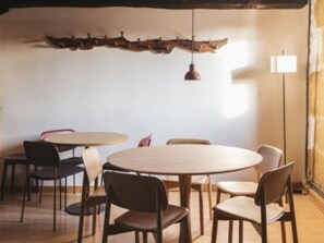 A room with round tables and chairs, a wooden ceiling feature, and a floor lamp.