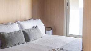 Ett hotellrum med en säng, kuddar, ett fönster och en dörr.