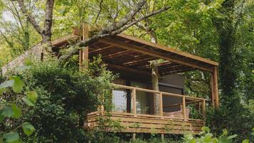 A wooden cabin with a balcony, surrounded by dense greenery.