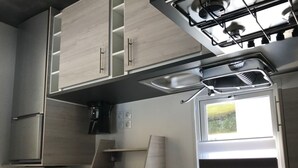Una cocina compacta con estufa a gas, armarios integrados, microondas y una ventana con persianas.