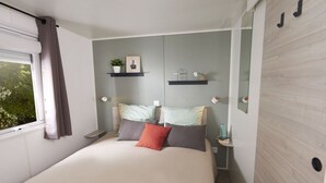 Un dormitorio con cama, ventana con cortinas, mesita de noche y repisas en la pared.