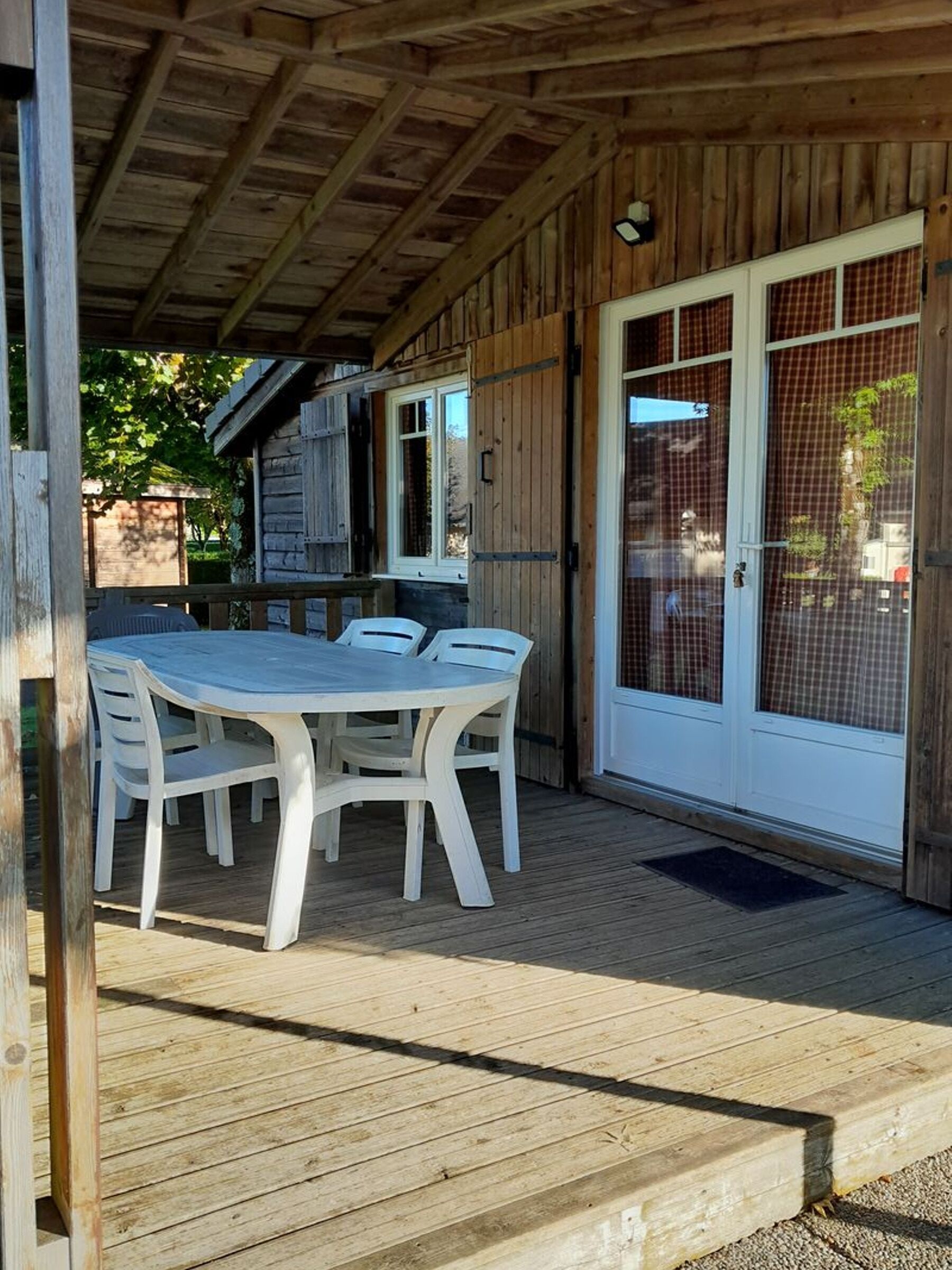Ein überdachter Außenbereich mit Holzdeck, einem weißen Tisch mit Stühlen und einer Glasglastür mit Metalldrahtgitter.