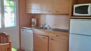Una cocina compacta con armarios de madera, lavavajillas integrado, microondas y pileta.