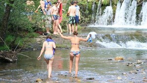 A natural setting with a waterfall and people in swimwear.