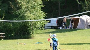A grassy field with a tent, a picnic table, and a person holding a tennis racket.