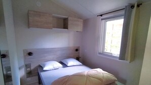 Ein Einzelbett mit Kopfteil, zwei Kissen, ein Nachttisch und ein Fenster mit Jalousien.