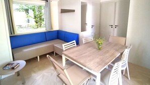 Ein modernes Zimmer mit einem Holztisch, weißen Stühlen, einer blauen gepolsterten Bank und einem kleinen Beistelltisch mit einem Buch.