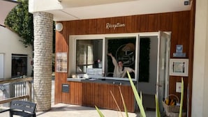 Zona de recepción con fachada de madera, un pilar de piedra y un ventanal con una persona en su interior.
