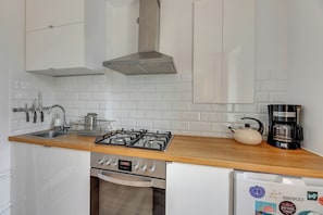 A kitchen with white cabinets, a stainless steel range hood, a gas stove, a coffee maker, and a dishwasher. - Surfer by Grand Apartments (Sopot)