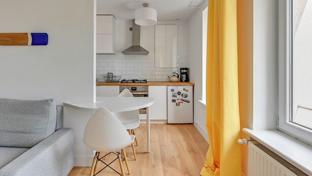 Ett kompakt bostadsutrymme med ett litet kök, en matplats och en soffa.