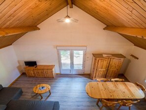 A loft-style room with a sloped ceiling, a wooden dining table with chairs, a sofa, a television, and a cabinet. - Cozy chalet for two, pets welcome (Méolans-Revel)
