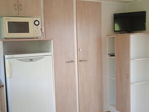 A room with a microwave, a refrigerator, and a television on a cabinet.