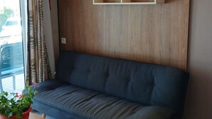A modern room with a wooden ceiling, a dark blue sofa, a wooden side table with a red pot, and a wall-mounted shelf.