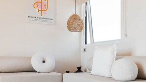 A modern living room with a sofa, a round white cushion, a woven pendant light, and a small wooden table with a bowl. - Bungalow with AC, pets allowed - 4 guests (Linguizzetta)