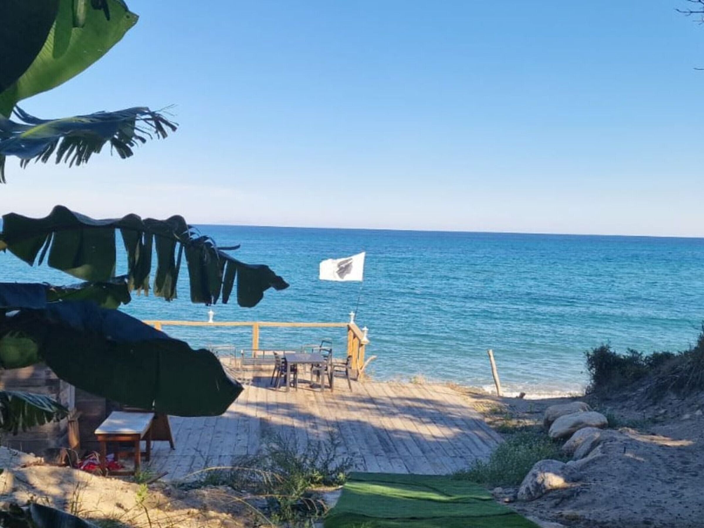 Een strand met een houten terras, een vlag en uitzicht op de oceaan.