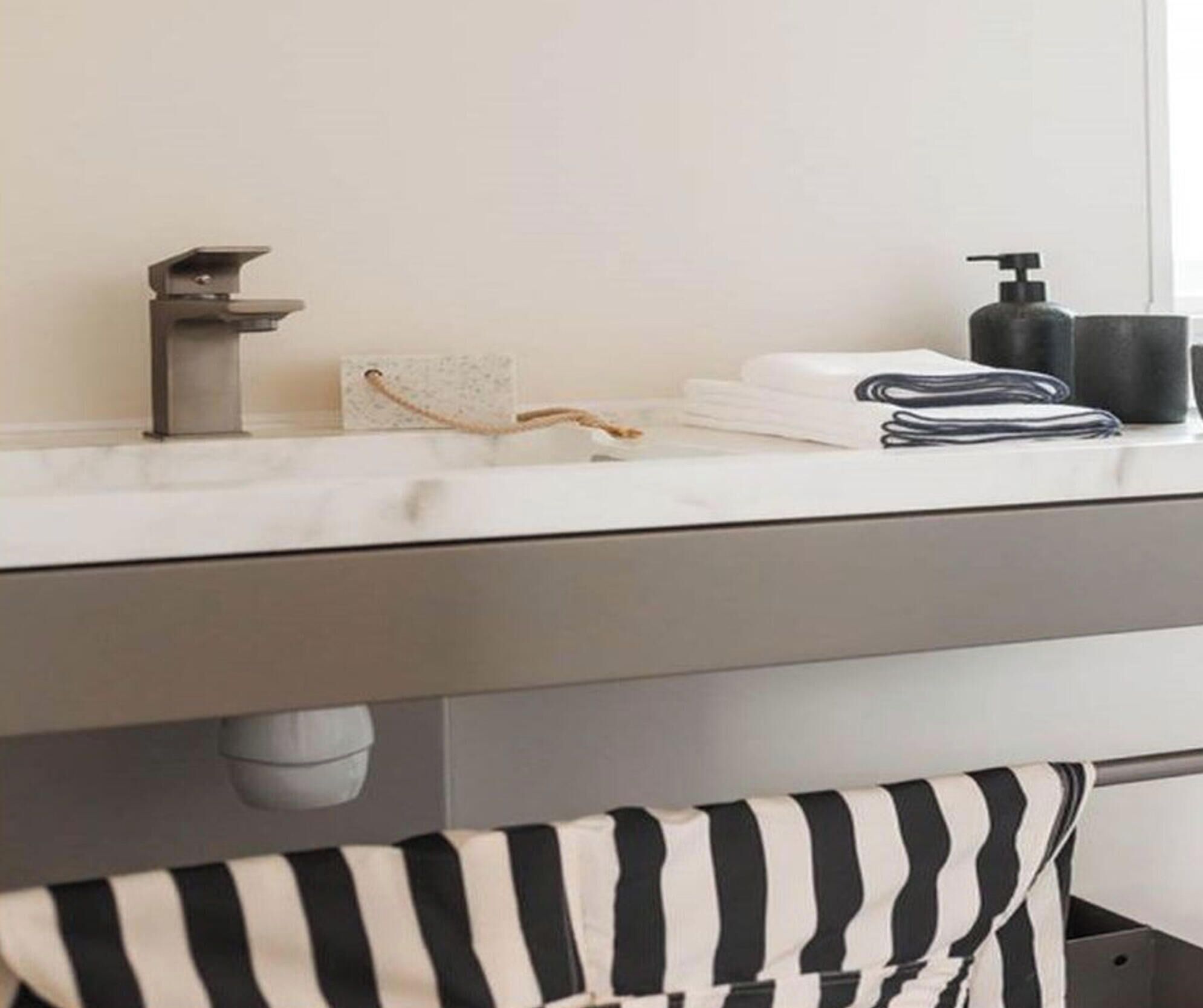 A bathroom with a white countertop, a towel rack, a soap dispenser, and a striped towel.