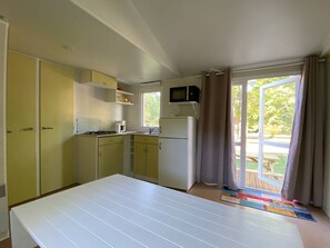 A compact kitchen with a microwave, refrigerator, and a window with curtains.