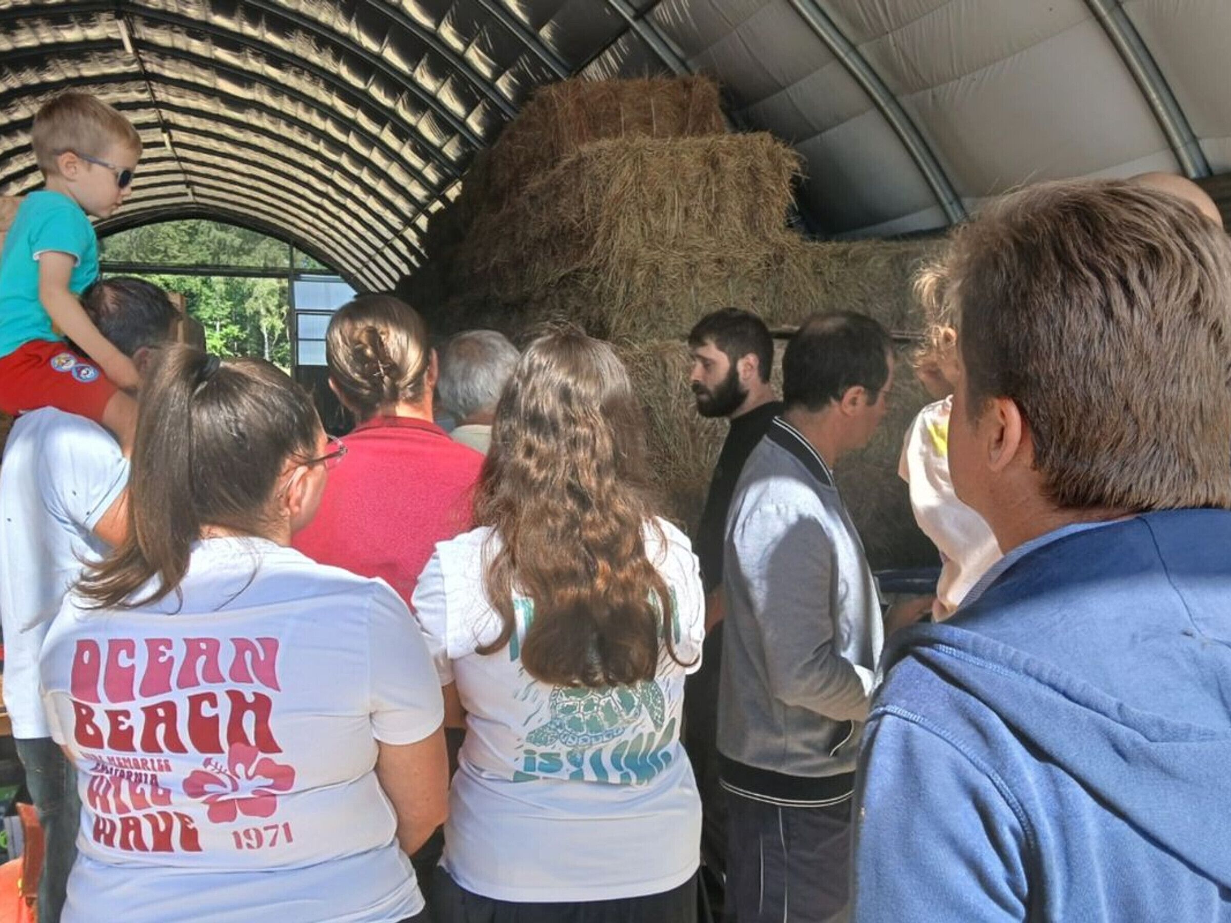 A group of people standing under a covered area with hay bales.