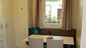 Ein Zimmer mit einem weißen Tisch, zwei weißen Stühlen, einem Fenster mit Vorhängen, einem kleinen Blumentopf und einer Tür mit einem Schild.