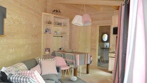 A cozy cabin interior with a sofa, dining table, and a small kitchen area. - Chalet with handicap access - 6 guests (Magné)