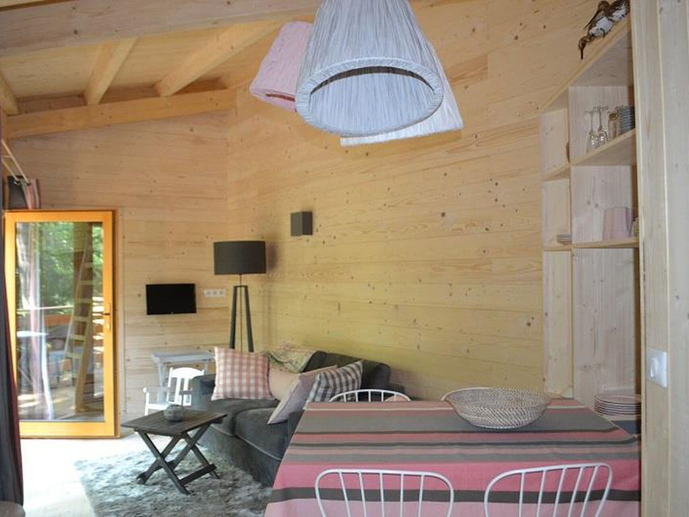 L’intérieur d’un chalet en bois, avec un canapé, une table à manger, des chaises, une lampe et une bibliothèque.
