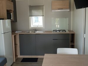 Eine kleine Küche mit Spüle, Herd und Schränken, ein Fenster mit Jalousien und ein weißer Stuhl.