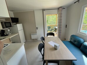 A compact room with a kitchenette, a dining table with chairs, a sofa, and a sliding door leading to an outdoor area. - Mobile home with AC, pets OK - 6 guests (La Chapelle-Aubareil)