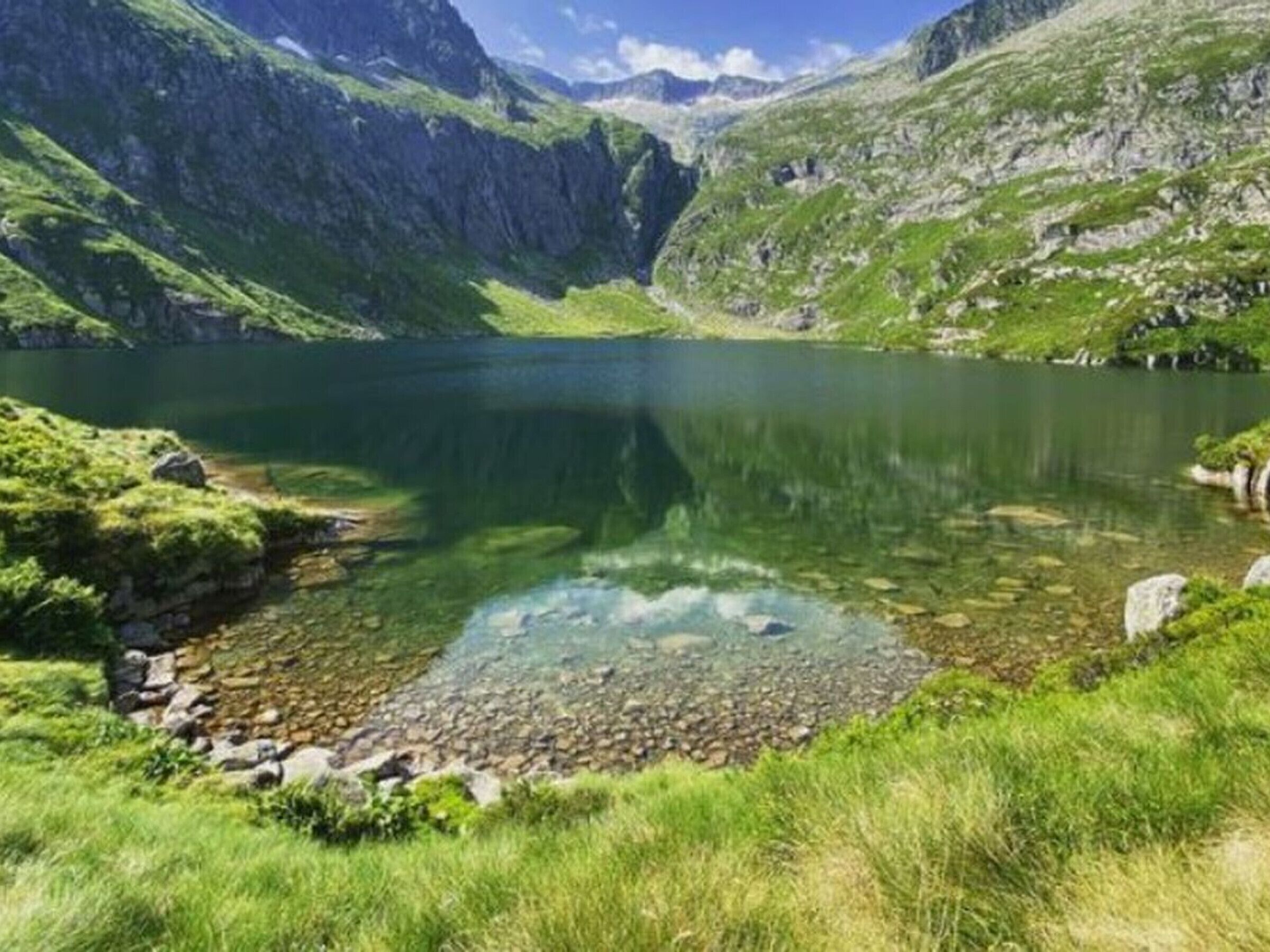 Un lago alpino limpido circondato da dolci colline ricoperte di verde.