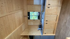 A compact wooden room with a built-in sink, cabinets, and a window.