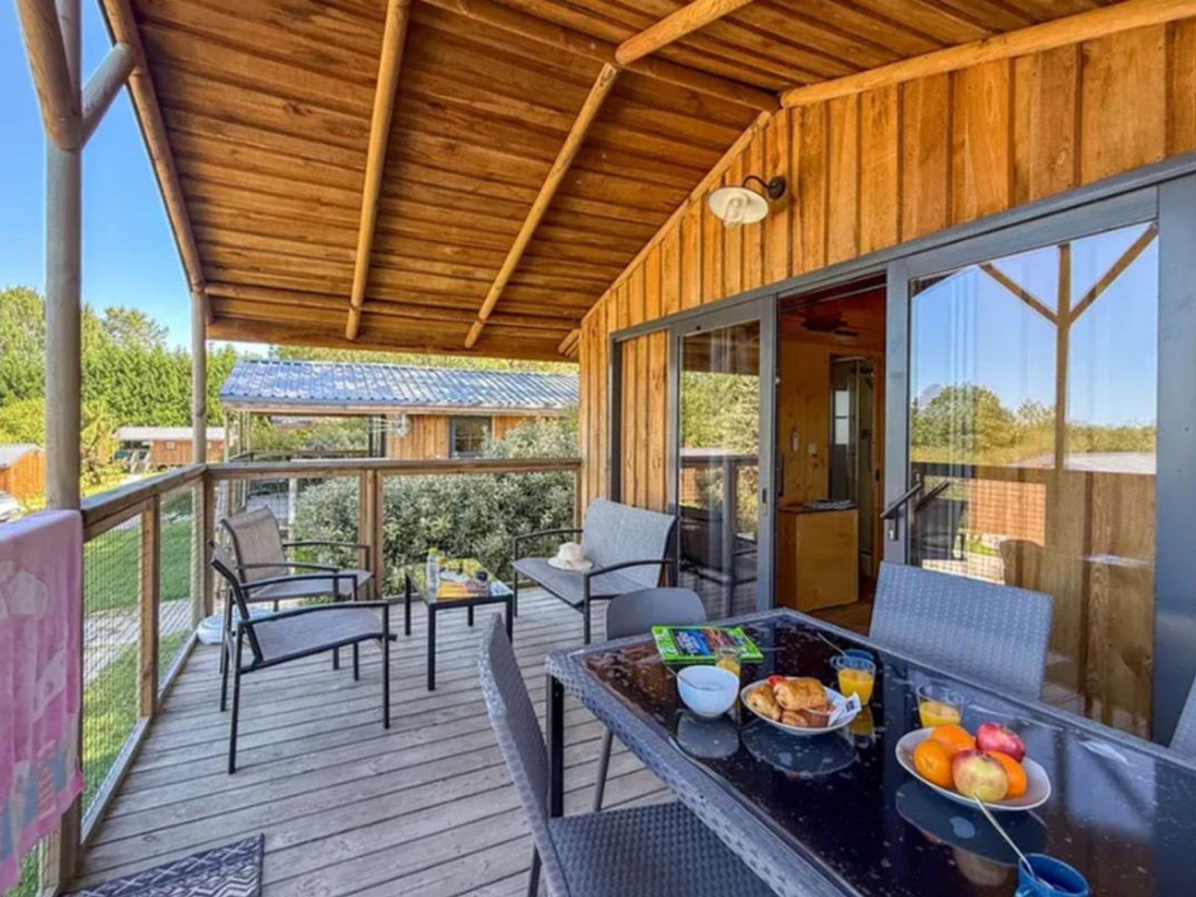 A covered outdoor area with a table set for breakfast, including fruits and a beverage.