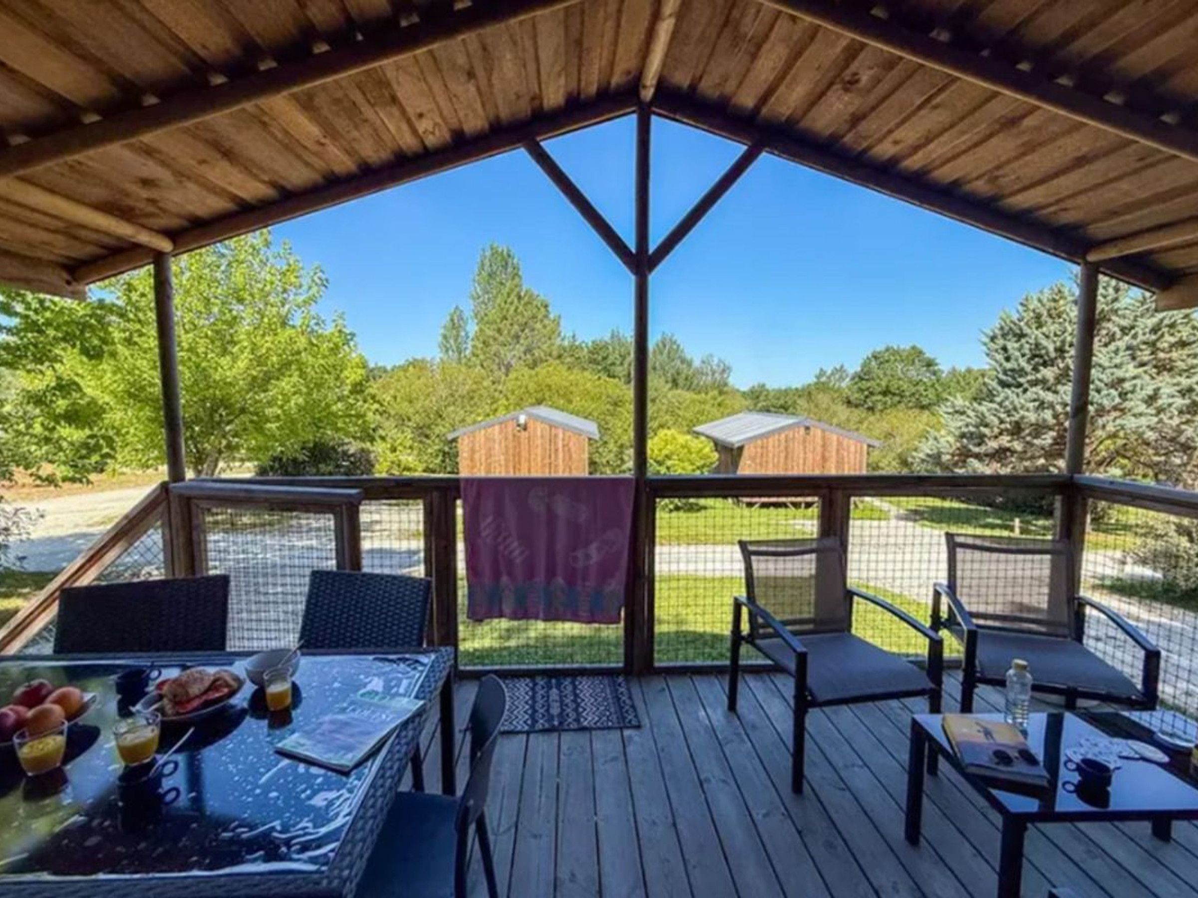 A covered outdoor seating area with tables and chairs, a view of the surrounding landscape, and a wooden structure in the background.