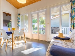 A room with a bed, a dining table with chairs, and large windows.