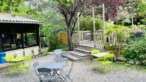 Un espace extérieur aménagé avec des tables et des chaises, protégé par un auvent et entouré de verdure, avec une terrasse en bois.