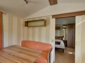 A room with a wooden table, orange sofa, striped walls, and a wooden-framed shelf. - Mobile home pets allowed - 1 guest (Saint-Cirq-Lapopie)