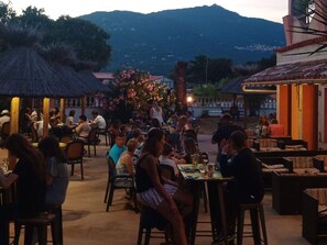 An outdoor dining area with tables and chairs, surrounded by buildings and a mountain in the background. - Mobile home with AC - 6 guests (Propriano)
