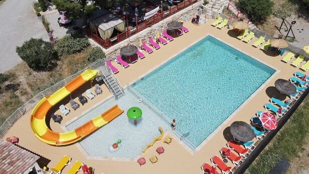 Ein Schwimmbecken mit Wasserrutsche, Liegestühlen und einer überdachten Sitzgelegenheit.