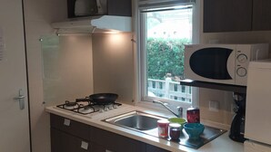 Eine kleine Küche mit Gaskochfeld, Mikrowelle, Spüle und einem Fenster mit Blick ins Grüne.