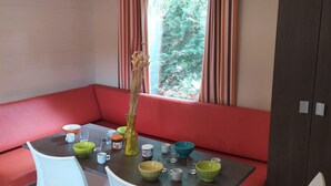 Ein Zimmer mit einem roten Sofa, einem runden Tisch mit Schalen und Tassen sowie einem Fenster mit gestreiften Vorhängen.