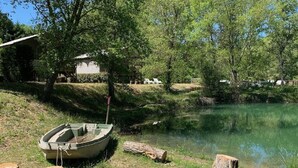 Ein Boot liegt an einem ruhigen Teich, umgeben von Bäumen und einem Gebäude im Hintergrund.